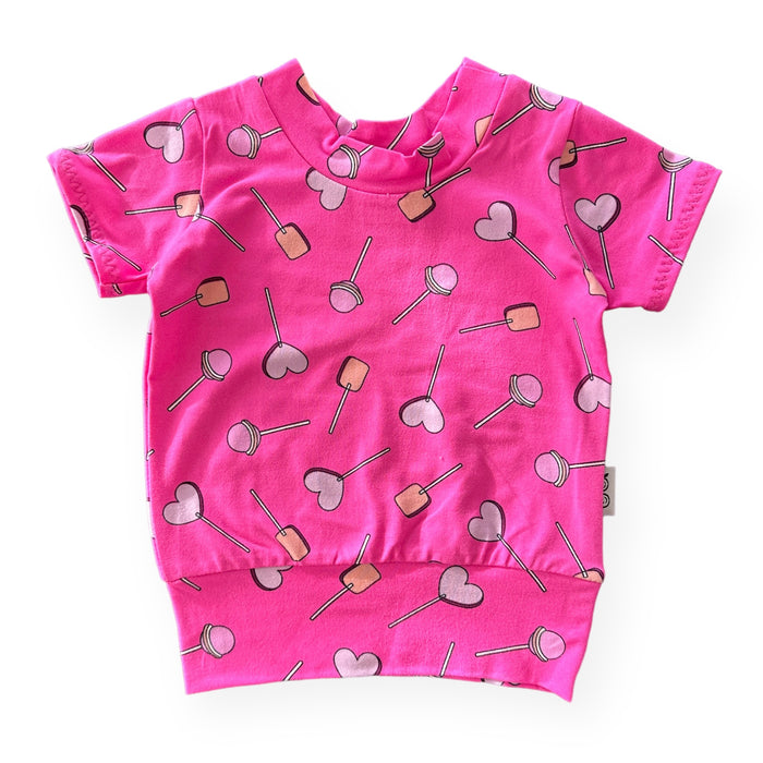 Handmade baby and toddler short-sleeve top featuring a vibrant pink lollipop and heart design. Soft, cozy, and perfect for pairing with leggings or pants for a playful yet comfortable look. Available in sizes preemie to 4T.